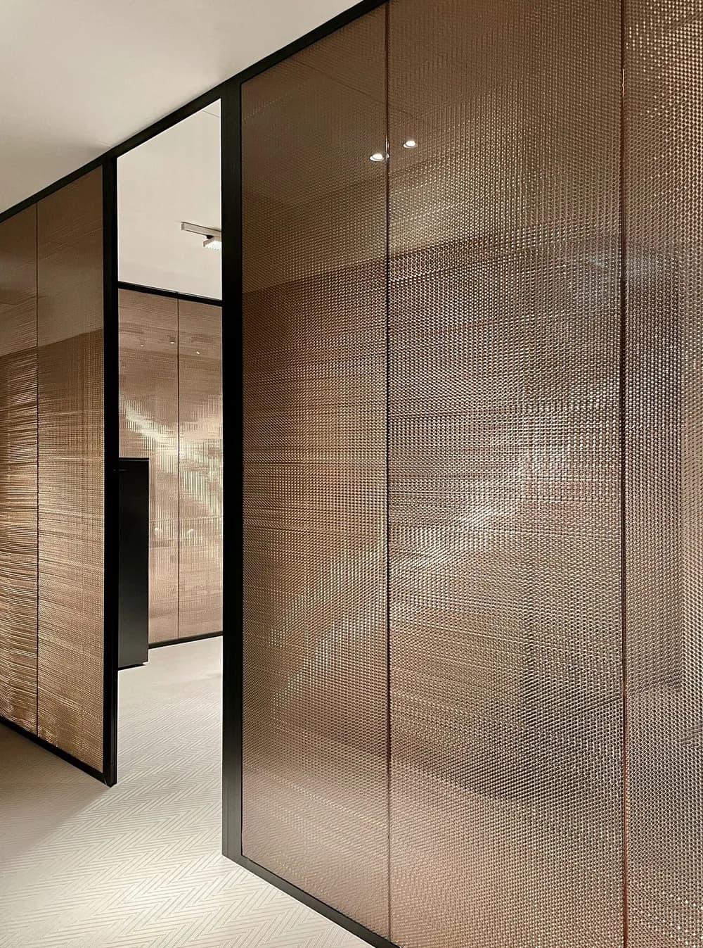 Fos partition wall in bronze honeycomb panels and dark profiles along an office corridor
