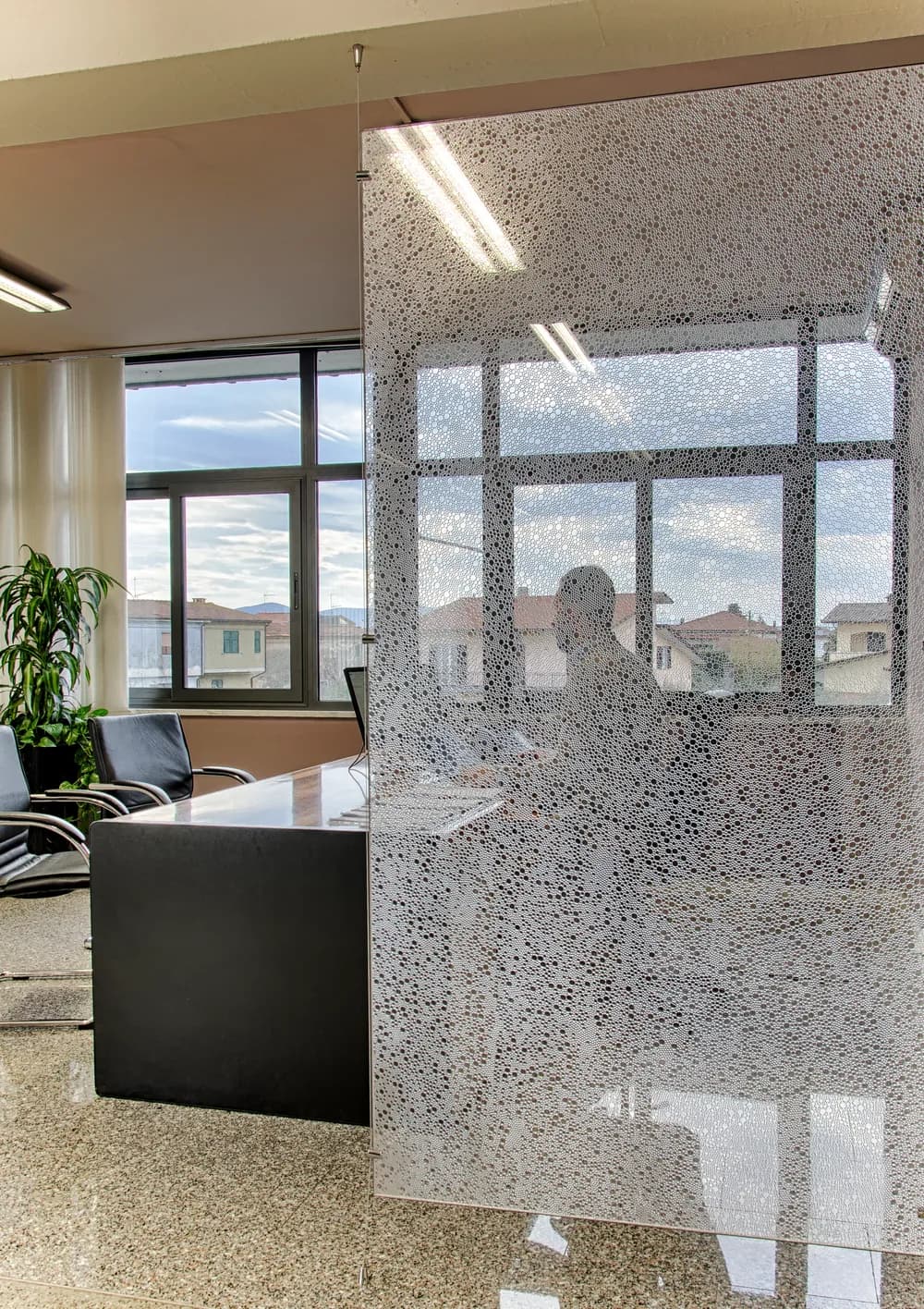 Stretch cable hung partition of bubble patterned panels dividing an open plan office with planters either side
