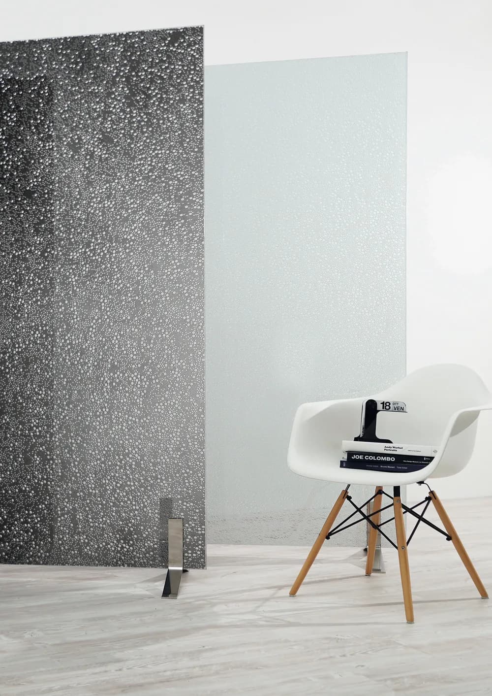 Three Upset freestanding panels in bronze, dark bubble pattern and satin clear on polished steel feet beside a white chair