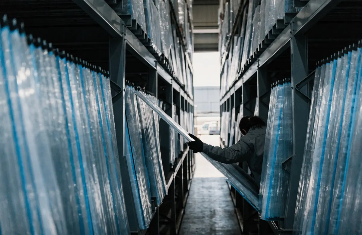 Full 4x8 acrylic sheets standing on edge in warehouse A-frame racks with blue masking film still on