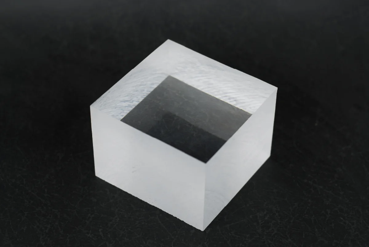 A thick block of clear cast acrylic on a dark surface, showing the optical clarity through the polished face and the frosted saw cut sides